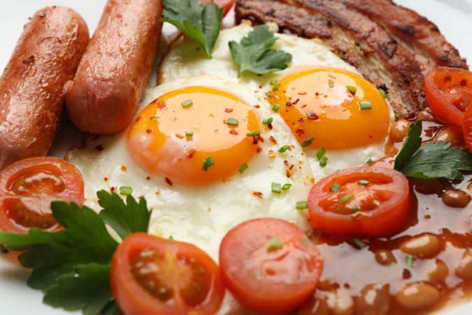Plate of breakfast with sunny side up eggs, tomatoes, sausage and bacon