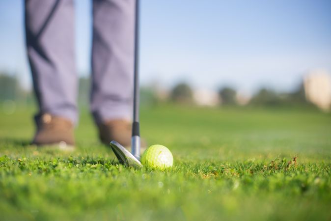 Cropped image of golf club and ball near person standing on green grass field
