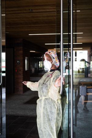 Nurse in PPE gestures for patient to come inside medical building