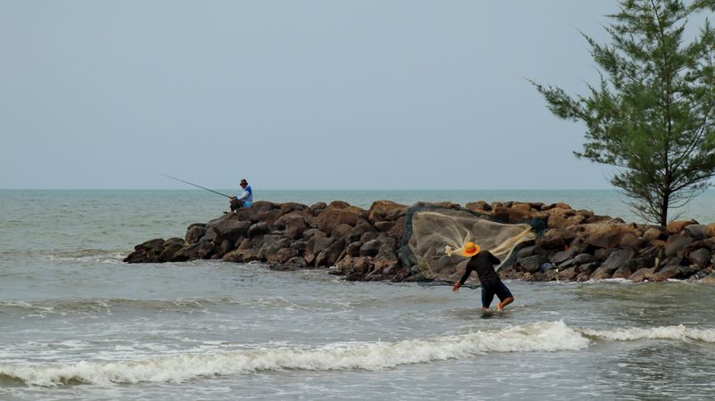 Two fishermen fishing with fishing rod and net on the beach