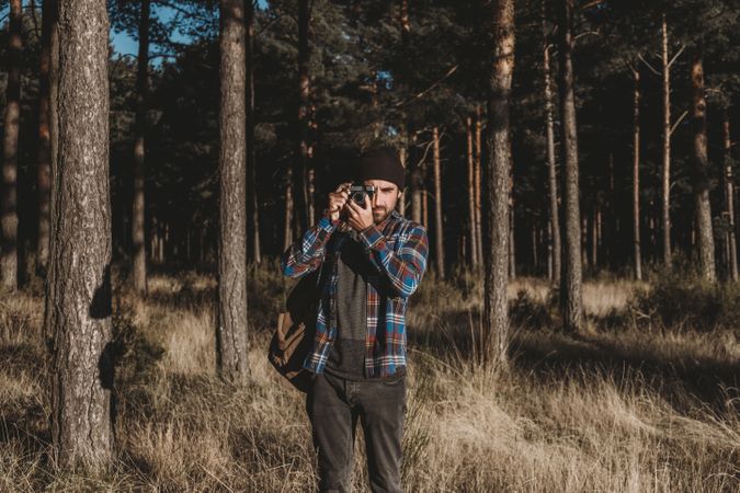 Confident photographer taking picture with camera in sunny forest