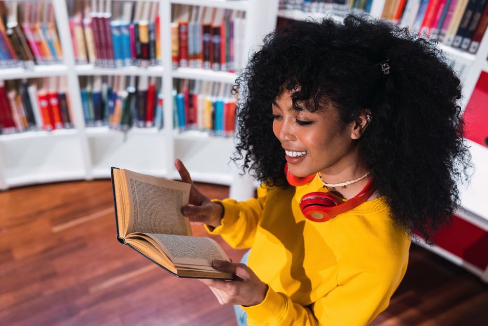 Content Black female student reading textbook in library
