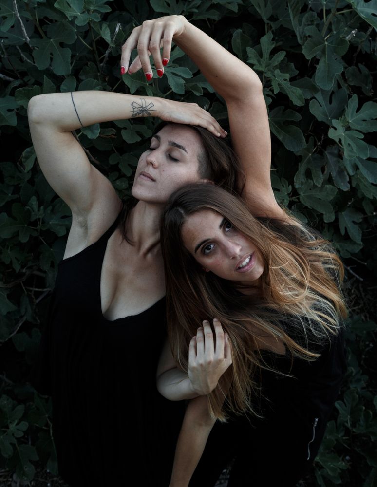 Young women posing near green bush