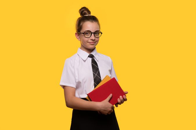Teen girl in school uniform holding books, wearing glasses