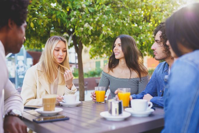 Diverse group of friends talking over coffee and juice at outside table