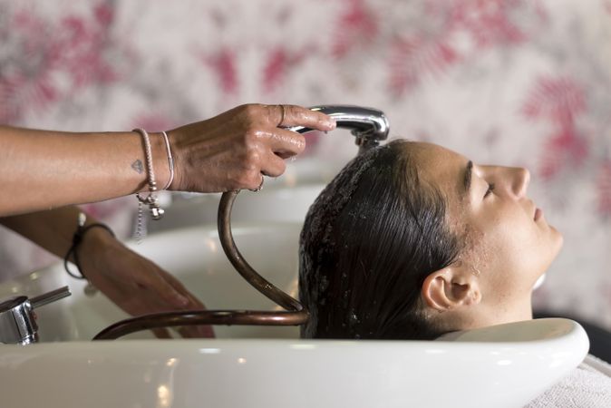 Female with head back in sink at hairdressers with a shower head rinsing her hair