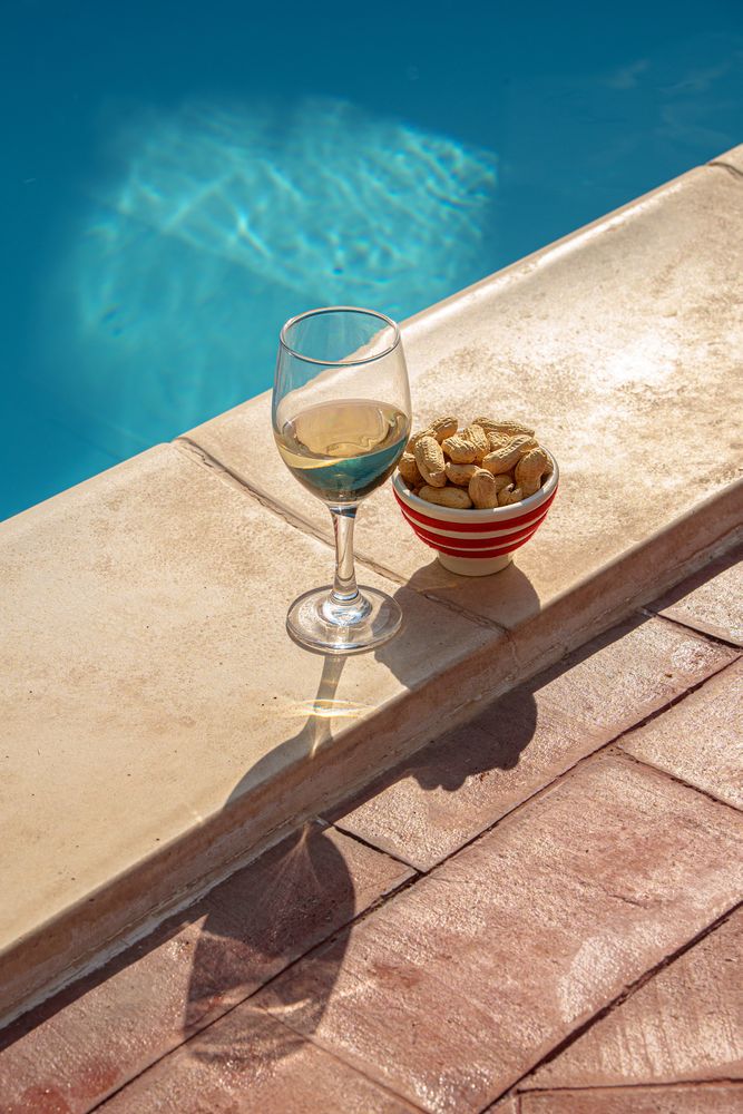 Glass of wine and a bowl of peanuts for an aperitivo by the pool in summer