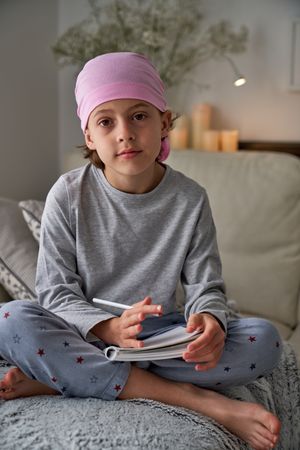 Barefoot boy in pink scarf writing in notepad