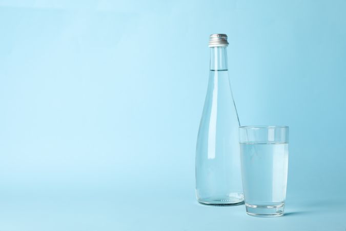 Water bottle with glass full of water in light blue space