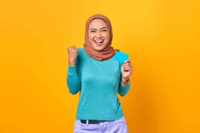 Muslim woman pointing holding credit card and making celebratory fist