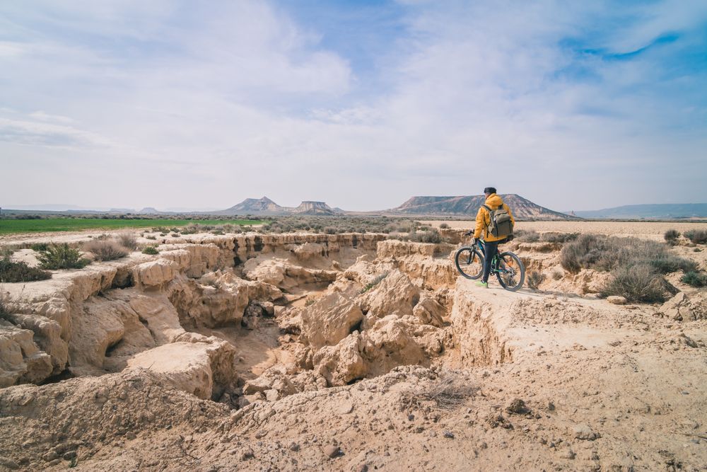 Man with bicycle standing on stone in desert hills