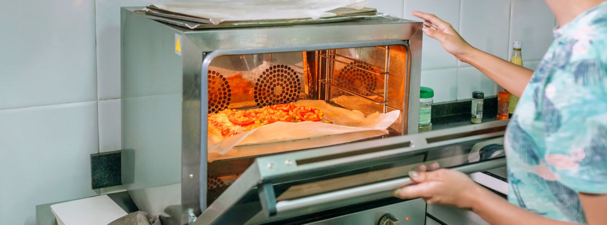 Unrecognizable professional cook opening oven door to take a pizza out in a restaurant kitchen