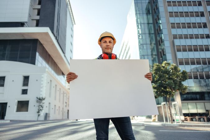 Construction worker looking at the camera while holding a blank placard in the city