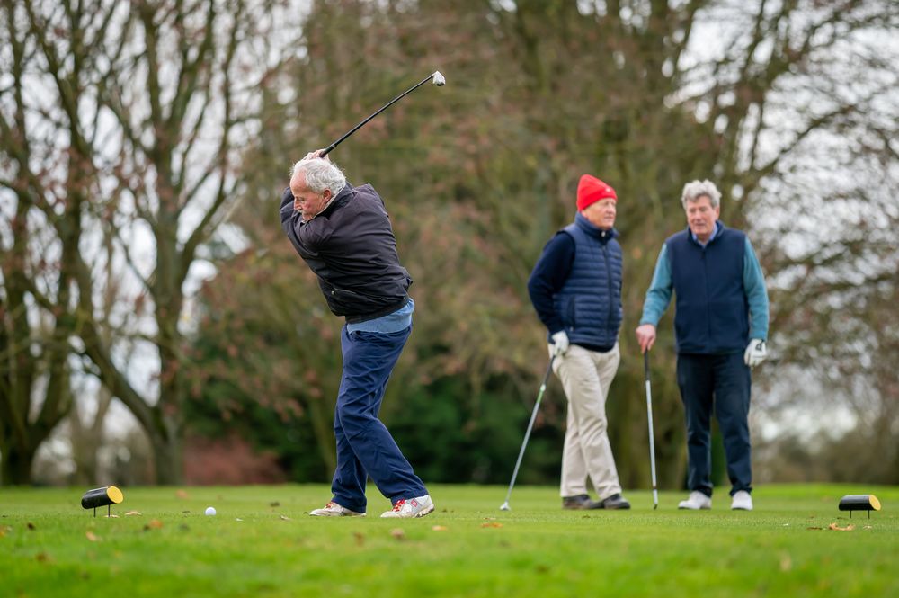 Man swinging on golf course with friends in background
