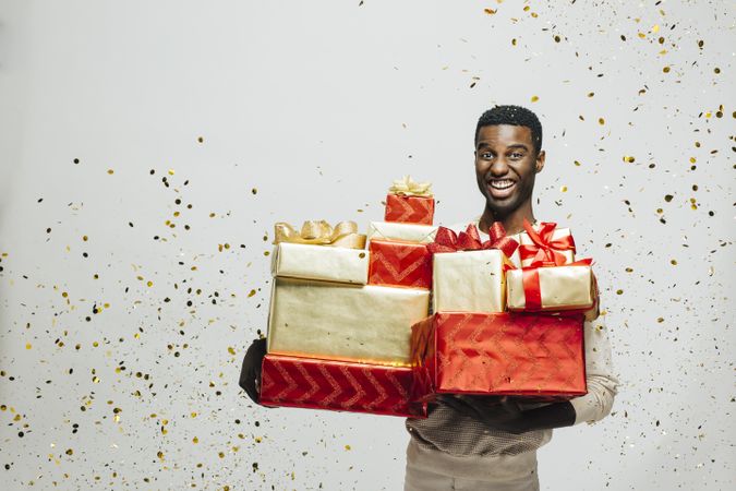 Smiling Black man holding pile of wrapped presents in both arms as glitter falls