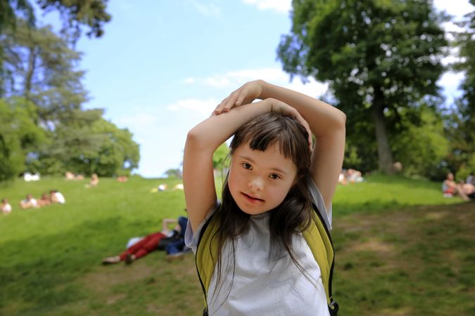 Young female child standing in a park with her arms above her head