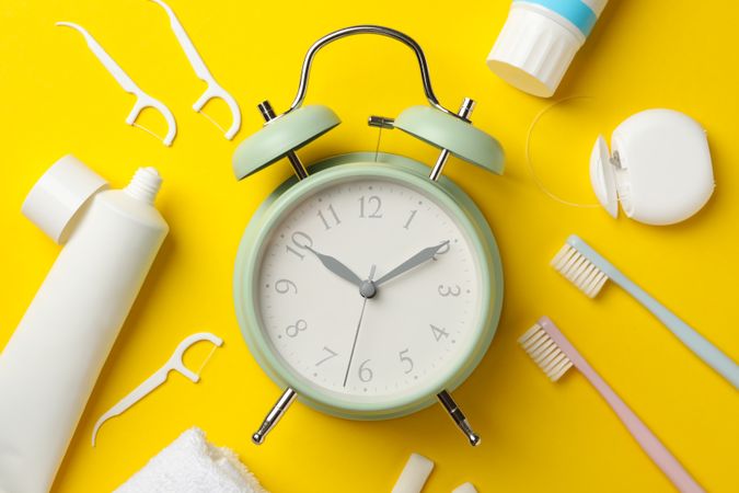 Alarm clock and dental care tools on yellow background, top view