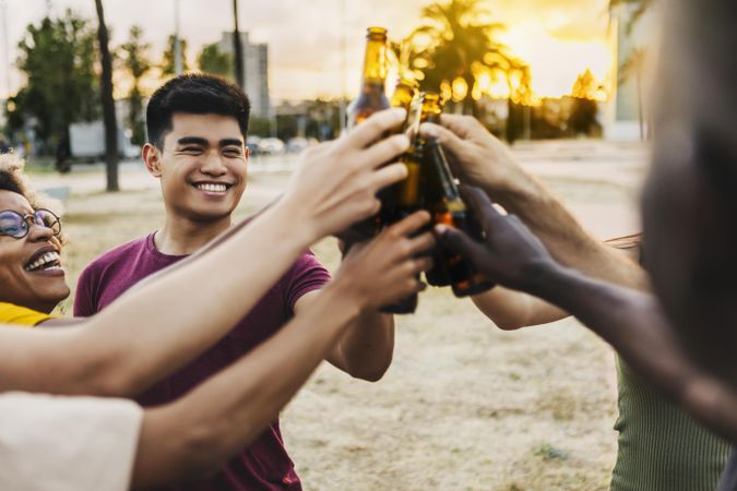 Multiracial friends celebrating and toasting beers at beach party