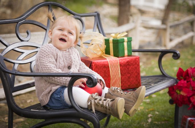 Young Toddler Child Sitting on Bench with Christmas Gifts Outside