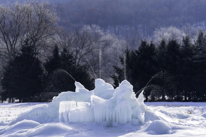 An ice fountain in the snow surrounded by trees