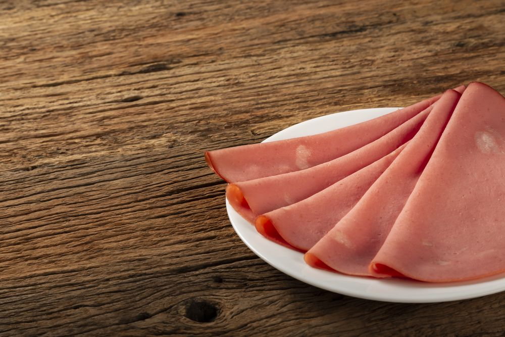 Plate with sliced mortadella on the table.