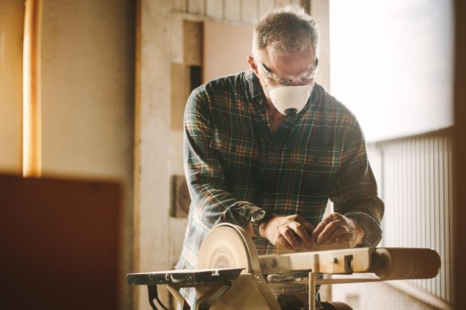 Male carpenter with face mask working on belt sander machine