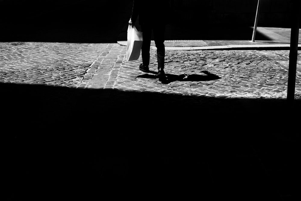 Feet of person crossing cobblestone road with shopping bag