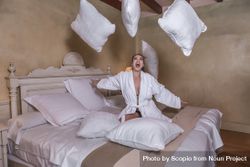 Excited woman in bathrobe throwing pillows in a hotel room 563zl4