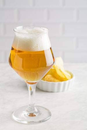 Glass of beer and chips on light background