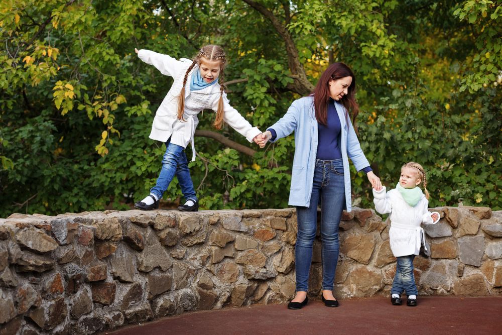 Mother with two girls walking along wall in park