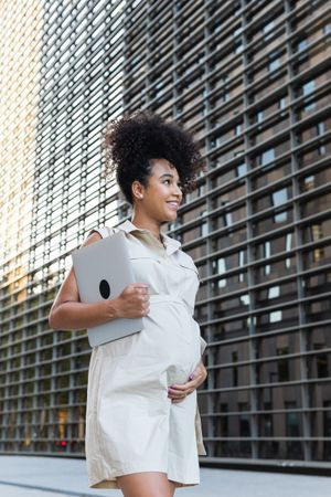 Smiling Black woman with laptop coming out of office building