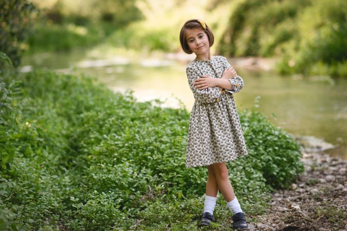 Child standing by river with her arms crossed