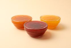 Bowls with jam on beige background, space for text