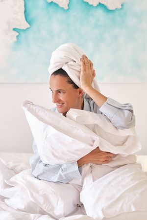 Smiling female hugging pillows on bed in morning