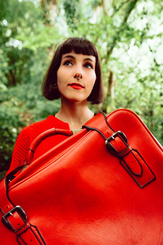 Woman in red with big red suitcase in forest