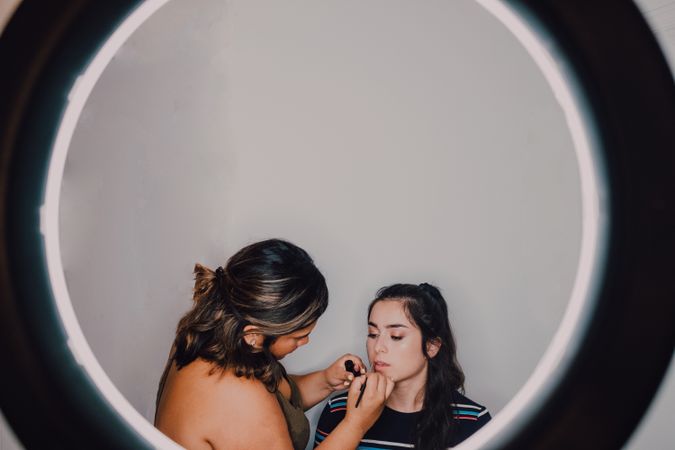 Professional visagiste putting makeup on young woman