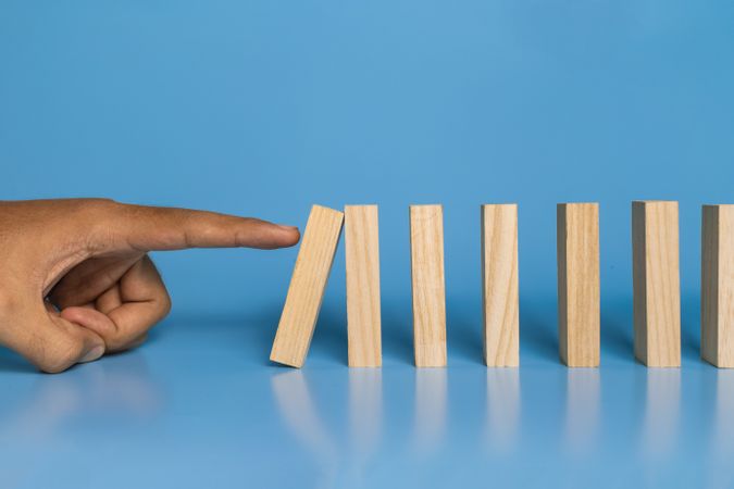 male hand drop wooden blocks isolated on blue background. domino effect or risk protection strategy concept