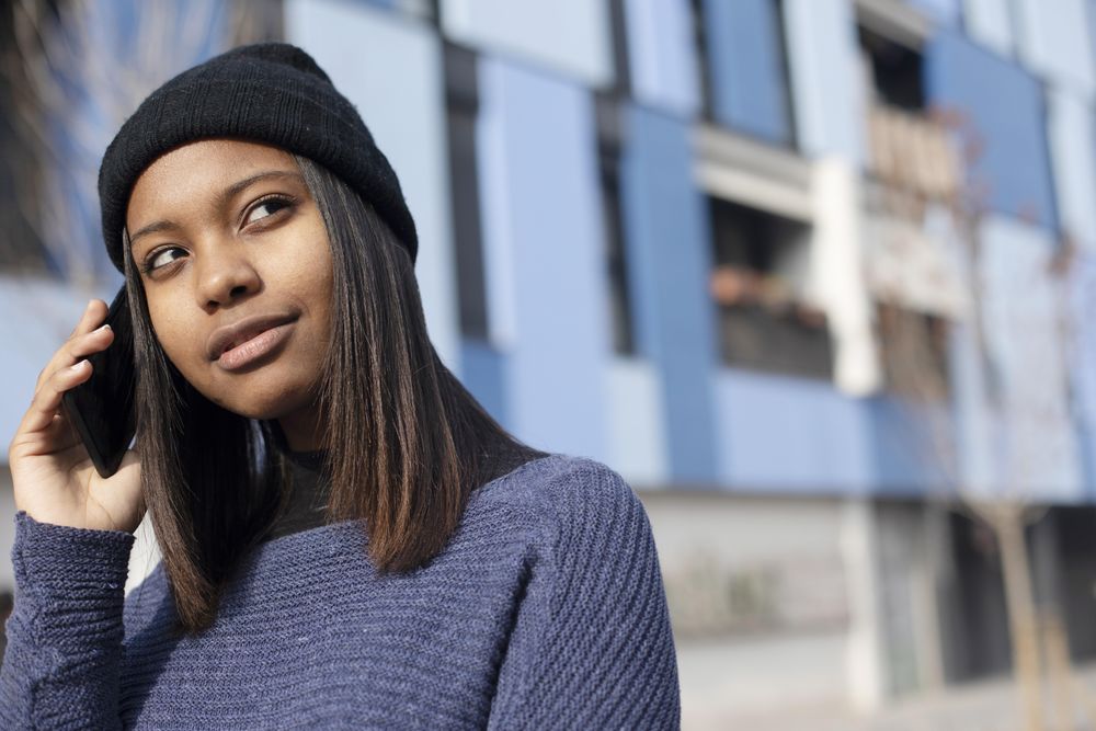 Content female in wool hat and blue sweater chatting on phone and looking to the side