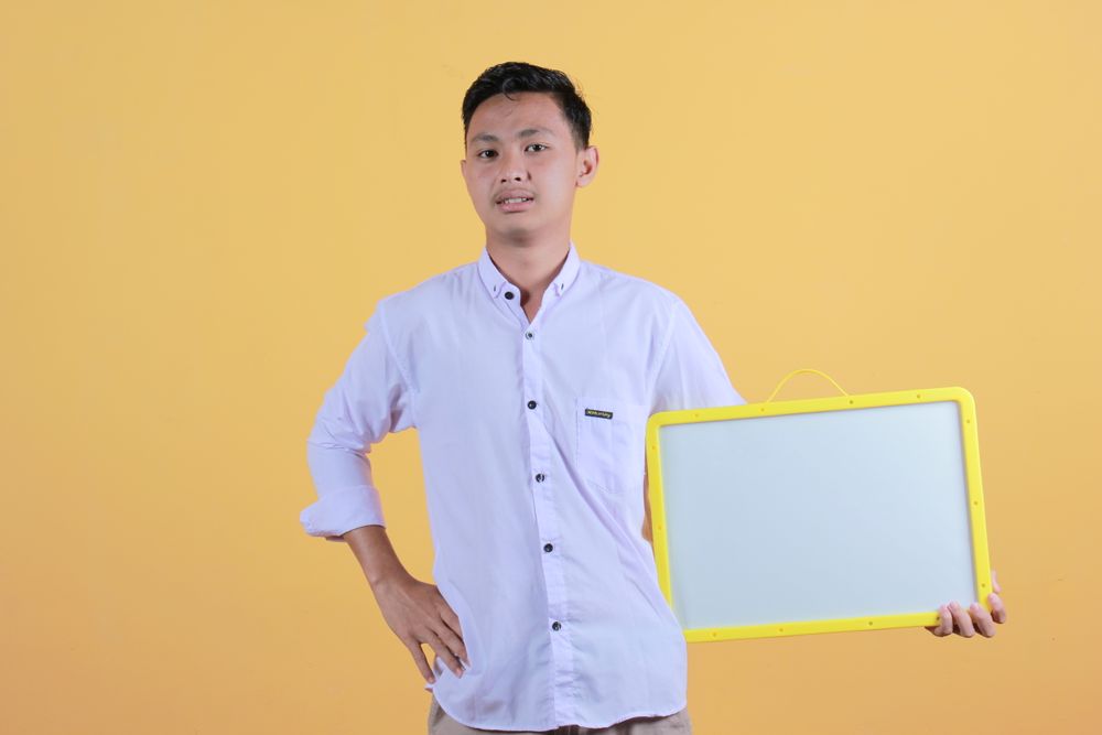 Portrait of a young man in yellow backdrop holding a blank note board