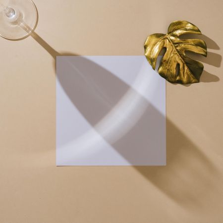 Shadow of wine glass with golden leaf and square paper on beige background