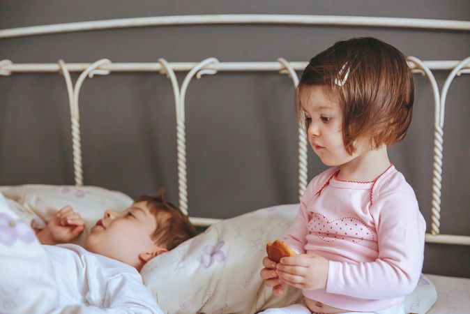 Closeup of thoughtful little girl holding cookie sitting in bed with brother on a relaxed morning
