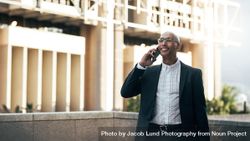 Man in business attire clothes standing on a building talking on mobile phone 4mnkWb