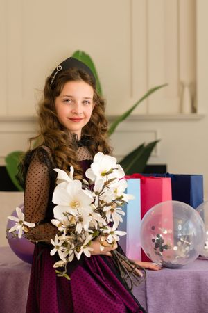 Girl holding flowers and balloons at birthday celebration.
