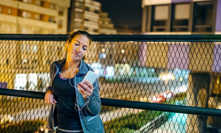 Portrait of young woman runner listening music on mobile phone application in evening
