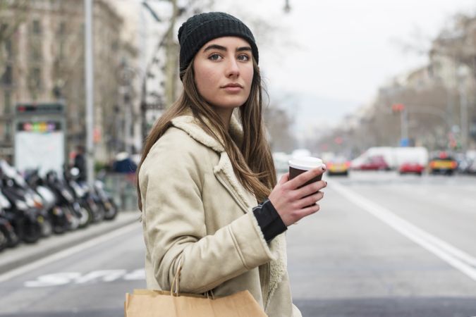 Portrait of woman crossing the street, with takeaway coffee and shopping bag