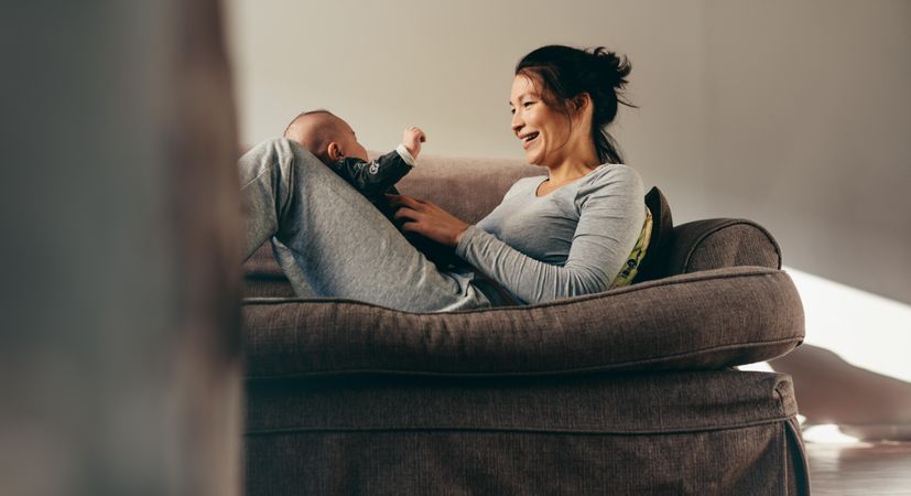 Smiling woman talking to her baby sitting on a couch at home
