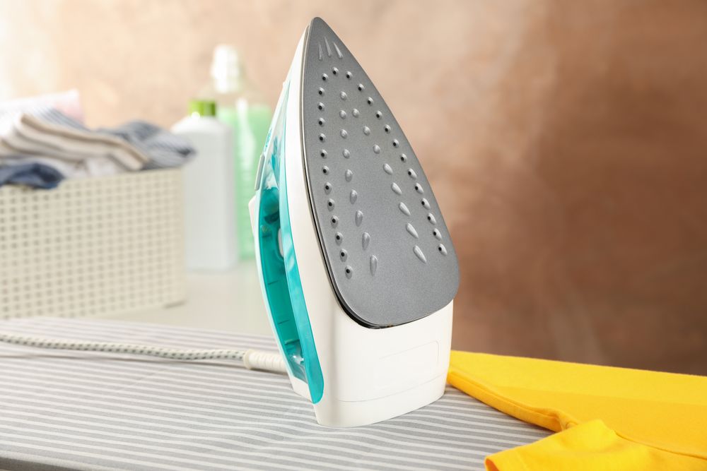 Iron and yellow t-shirt on ironing board, space for text