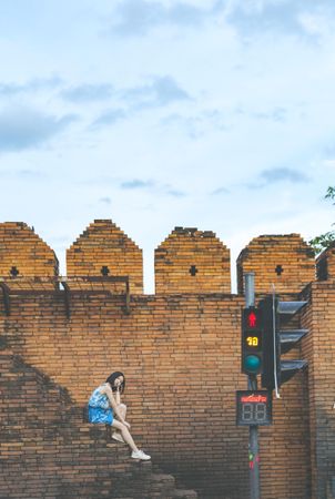 Woman sitting on outdoor brown brick stairs near traffic light