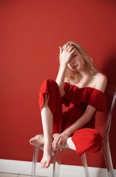 Beautiful young adult woman wearing red jumpsuit relaxing in studio