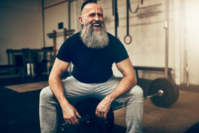 Laughing man with big grey beard sitting in weightlifting gym